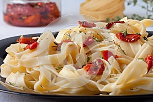 Fettuccine pasta with sun-dried tomatoes and rosemary is lying on a black plate. Close up