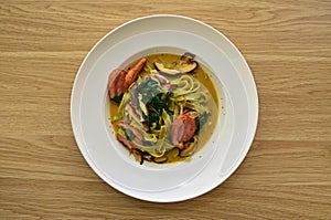 Fettuccine pasta in tasty broth fresh green wilted spinach and slices of smoked duck