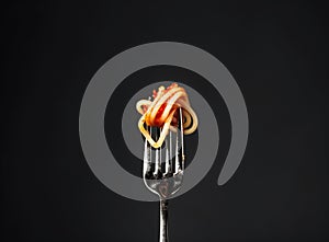 Fettuccine pasta with tomato sauce on fork against black background, closeup.