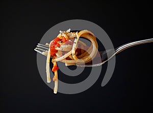 Fettuccine pasta with tomato sauce on fork against black background, closeup.