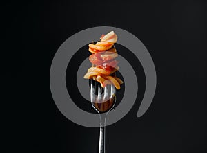 Fettuccine pasta with tomato sauce on fork against black background, closeup.