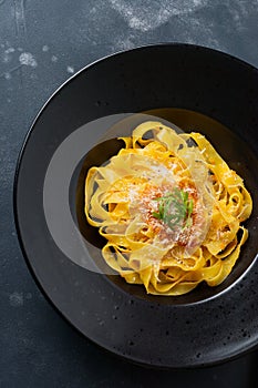 Fettuccine pasta with traditional Italian Passat sauce and parmesan cheese in black plate on dark background.