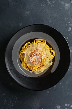 Fettuccine pasta with traditional Italian Passat sauce and parmesan cheese in black plate on dark background.