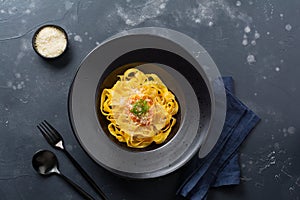 Fettuccine pasta with traditional Italian Passat sauce and parmesan cheese in black plate on dark background.