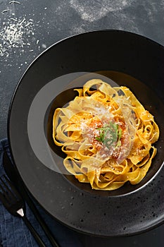 Fettuccine pasta with traditional Italian Passat sauce and parmesan cheese in black plate on dark background.