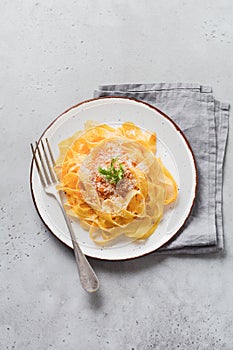 Fettuccine pasta with traditional Italian Passat sauce and parmesan cheese in light plate on old white concrete background.