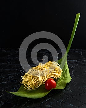 Fettuccine raw italian pasta on a green leaf with cherry tomato