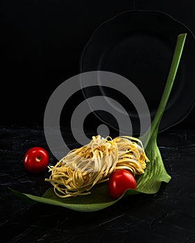 Fettuccine raw italian pasta on green leaf with cherry tomatoes