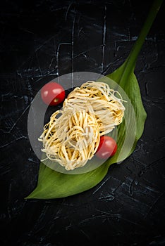 Fettuccine raw italian pasta on green leaf with cherry tomatoes