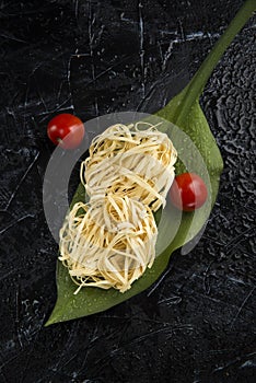 Fettuccine raw italian pasta on green leaf with cherry tomatoes