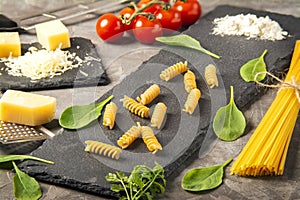 Fettuccine and spaghetti with ingredients for cooking pasta, tomato, arugula on black rock plate.