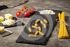 Fettuccine and spaghetti with ingredients for cooking pasta, tomato, arugula on black rock plate.