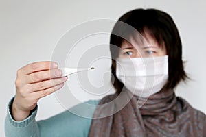 Fever and coronavirus, woman with a scarf wrapped around her throat measures body temperature