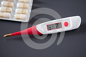 Fever thermometer and pills on the desk, 38 degrees Celsius on the display