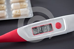 Fever thermometer and pills on the desk, 38 degrees Celsius on the display