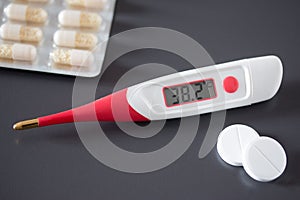 Fever thermometer and pills on the desk, 38 degrees Celsius on the display