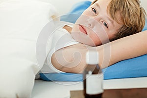 Feverish boy in bed next to medicine bottle