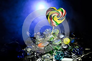 Few colorful candy heart lollipops on different colored candies against dark toned foggy background.