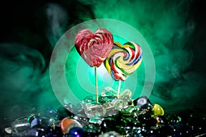 Few colorful candy heart lollipops on different colored candies against dark toned foggy background.