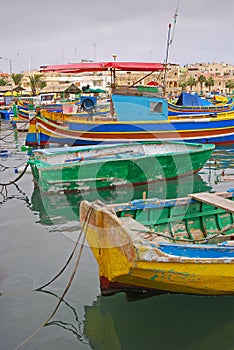 Few colourful traditional Maltese fishing boat Luzzu anchored with old houses behind at cloudy fishing village Marsaxlokk, Malta