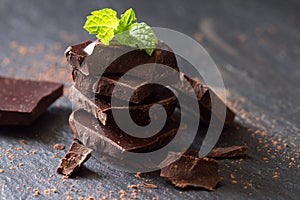 A few cubes of dark chocolate with mint leaves on black background