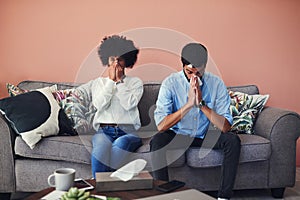 A few days later he got sick too. Shot of a young couple blowing their noses while sitting on the sofa at home.