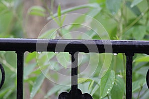 Few drops of rain water rolls down the rail installed in front of a house. Spherical shaped droplet is crystal transparent