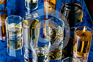 A few glasses of different sizes, filled with different whiskey shot on a mirror in a bar.