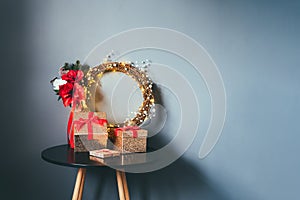 Few glittering golden gift boxes with velvet red ribbon and elegant Christmas flower wreath on the black table on gray