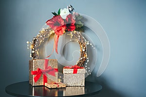 Few glittering golden gift boxes with velvet red ribbon and elegant Christmas flower wreath on the black table on gray