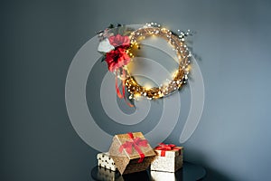 Few glittering golden gift boxes with velvet red ribbon and elegant Christmas flower wreath on the black table on gray