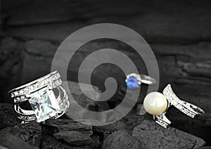 Few jewelry rings with brilliants, gems and pearl on dark coal b photo