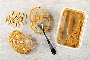 Few of peanut, sandwich with peanut butter, spoon with paste on bread, container with peanut butter on table. Top view