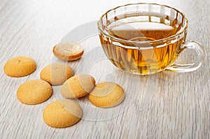 Few round biscuits, transparent cup with tea on wooden table