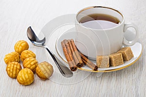 Few round cookies, teaspoon, tea, cinnamon sticks, sugar on saucer