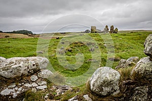 A few rounded stones with scrubby grass in the foreground and the ruins of Finlaggan castle on a deep green rolling grassy field