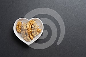 A few shelled walnuts lie in a saucer in the shape of a heart on textured slate board