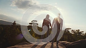 Few shots of adorable couple in casual clothes holding their hands on the high rocky mountain hill surrounded by green