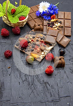 A few slices of chocolate, berries, flowers, and a basket of strawberry leaves on a black slate background