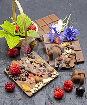 A few slices of chocolate, berries, flowers, and a basket of strawberry leaves on a black slate background