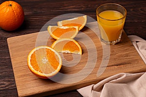 Few slices of orange and a glass of juice on a wooden cutting board
