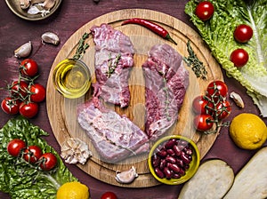 Few slices of raw beef on a cutting board, around lie ingredients tomatoes on a branch, lemon, olive oil, red hot pepper, herbs, l