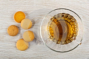 Few small biscuits, cup with tea on saucer on wooden table. Top view