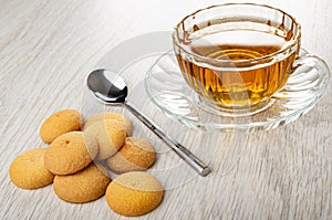 Few small biscuits, poon, transparent cup with tea on wooden table