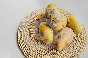 few spoiled over-ripe yellow mangoes with patches of rot and bedsores on round woven eco-napkin. improper storage of food