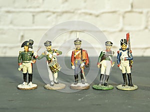 A few tin soldiers stand on a gray surface against a brick wall