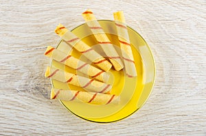 Few wafer rolls in yellow saucer on wooden table. Top view