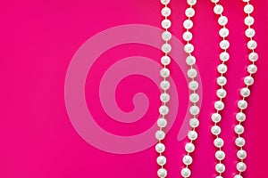 Few white pearl beads threadson a bright pink background. Glamorous background for processing