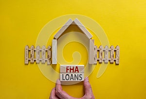 FHA loans symbol. Words `FHA loans` on blocks. Male hand, wooden fence, model of a house. Business and FHA - federal housing