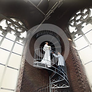 Fiance helps bride to go down on the spiral stairs in old Gothic